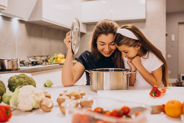 Mother with little daughter cooking together at kitchen